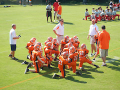 Amerikkalaista jalkapalloa pelaavat lapset ovat kerääntyneet kuuntelemaan valmentaja- ja huoltajajoukon ohjeita.