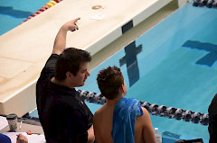 Valmentaja keskustelee valmennettavansa kanssa uima-altaan reunalla.